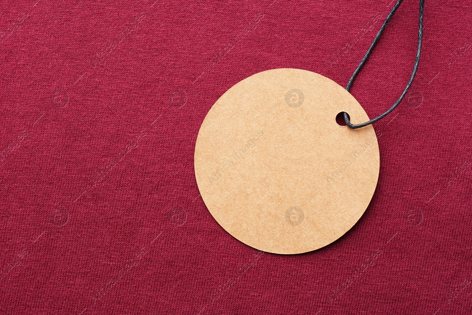 Photo of Circle shaped tag with space for text on dark red fabric, top view