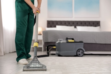 Photo of Professional janitor removing dirt from carpet with vacuum cleaner in bedroom, closeup. Space for text