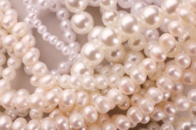 Elegant pearl necklaces on beige background, top view
