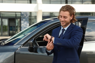 Photo of Attractive young man checking time near luxury car outdoors