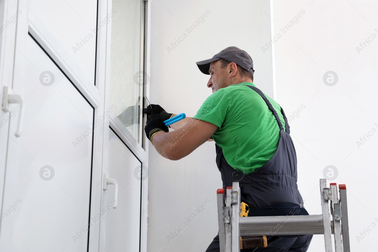 Photo of Worker on folding ladder installing window indoors