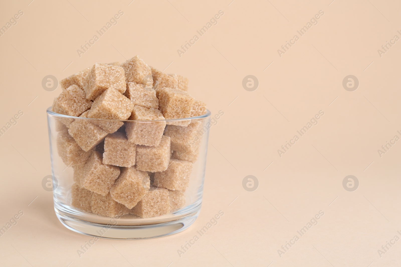 Photo of Brown sugar cubes in glass on beige background, closeup. Space for text