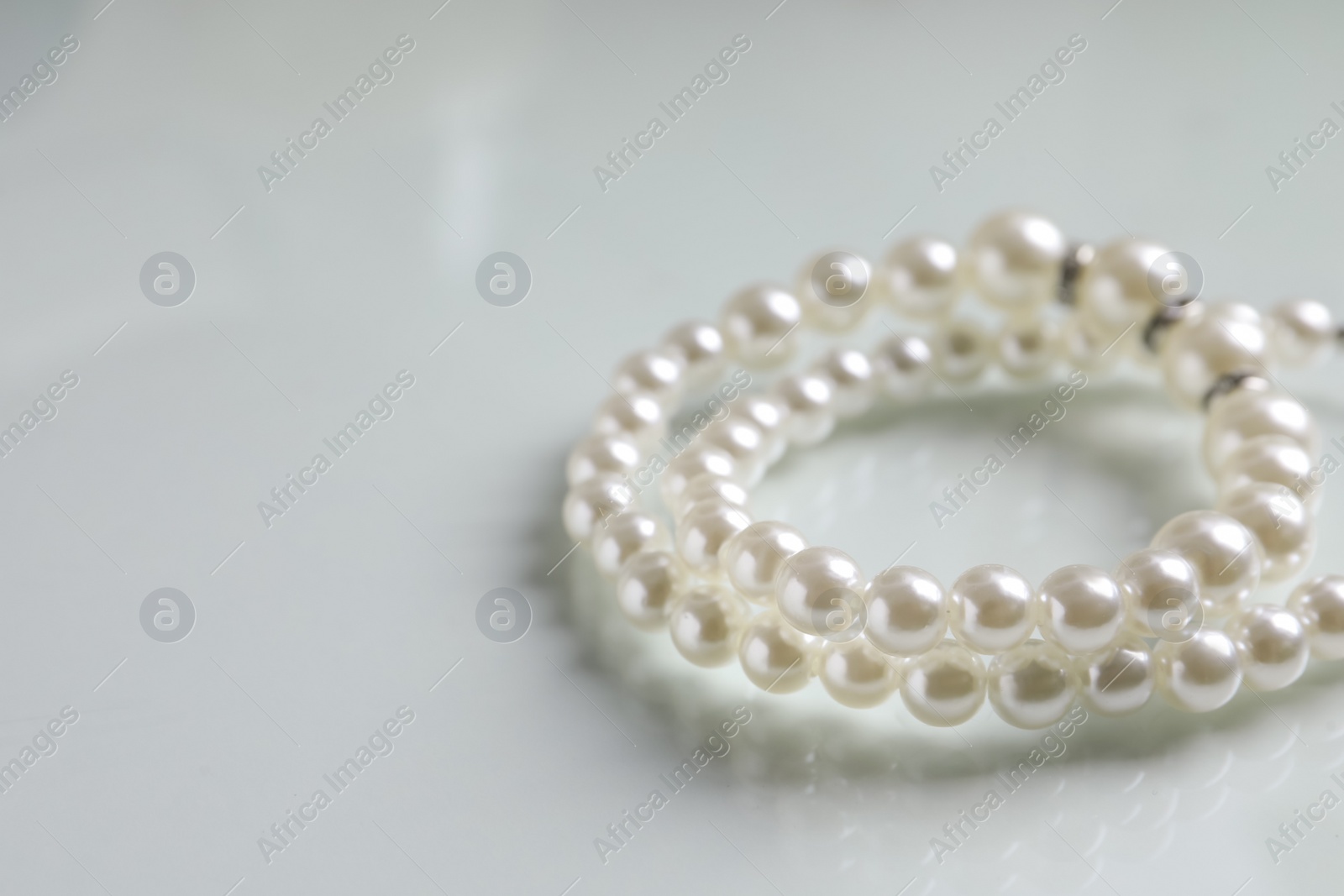 Photo of Elegant pearl necklace on white table, closeup. Space for text