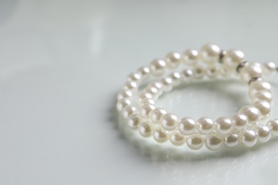 Elegant pearl necklace on white table, closeup. Space for text