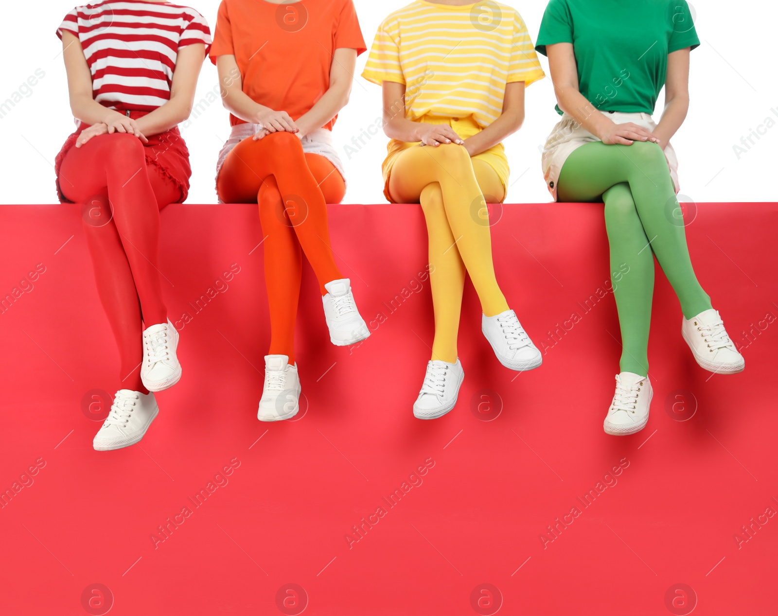 Photo of Women wearing bright tights sitting together on color background, closeup