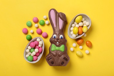 Photo of Chocolate Easter bunny, halves of egg and candies on yellow background, flat lay