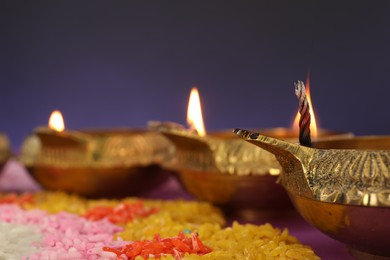 Photo of Diwali celebration. Diya lamps and colorful rangoli against purple background, closeup