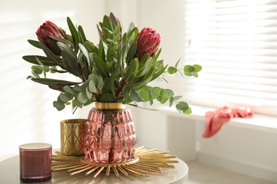 Vase with bouquet of beautiful Protea flowers on table in room