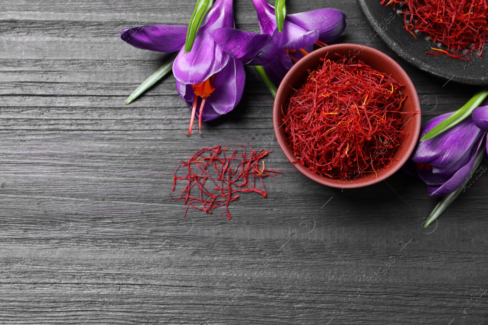 Photo of Dried saffron in bowl and crocus flowers on black wooden table, flat lay. Space for text