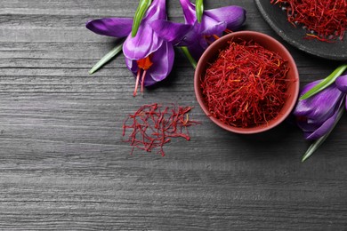 Photo of Dried saffron in bowl and crocus flowers on black wooden table, flat lay. Space for text