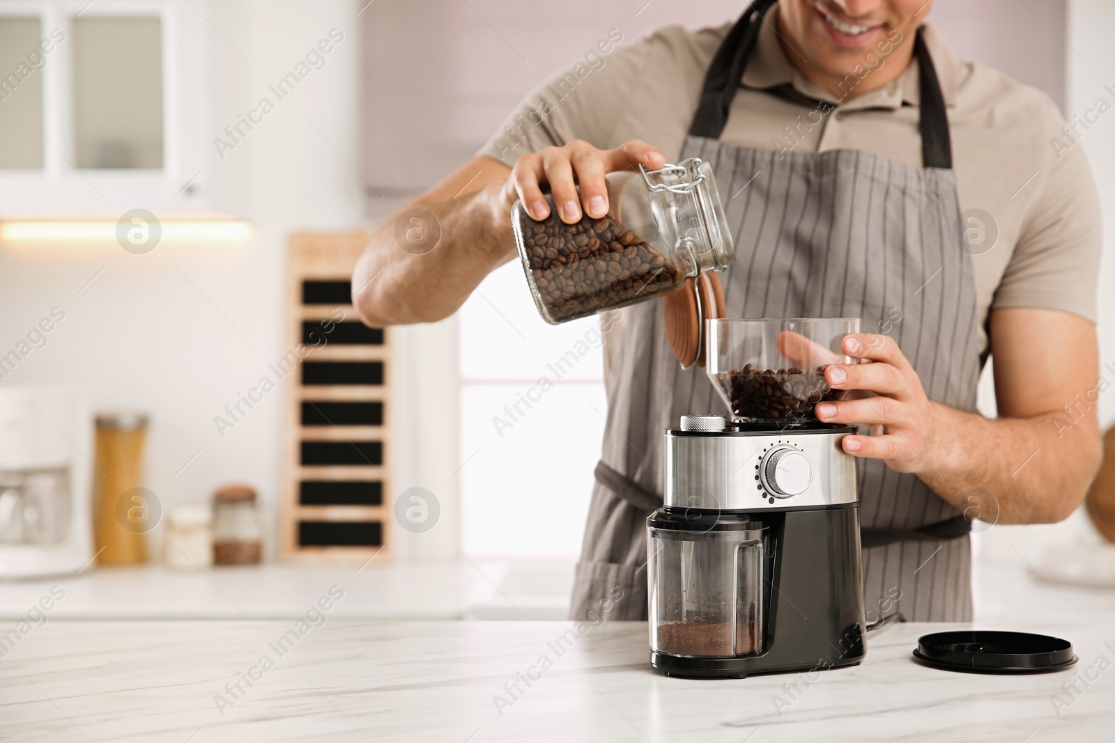 Photo of Man using electric coffee grinder in kitchen, closeup