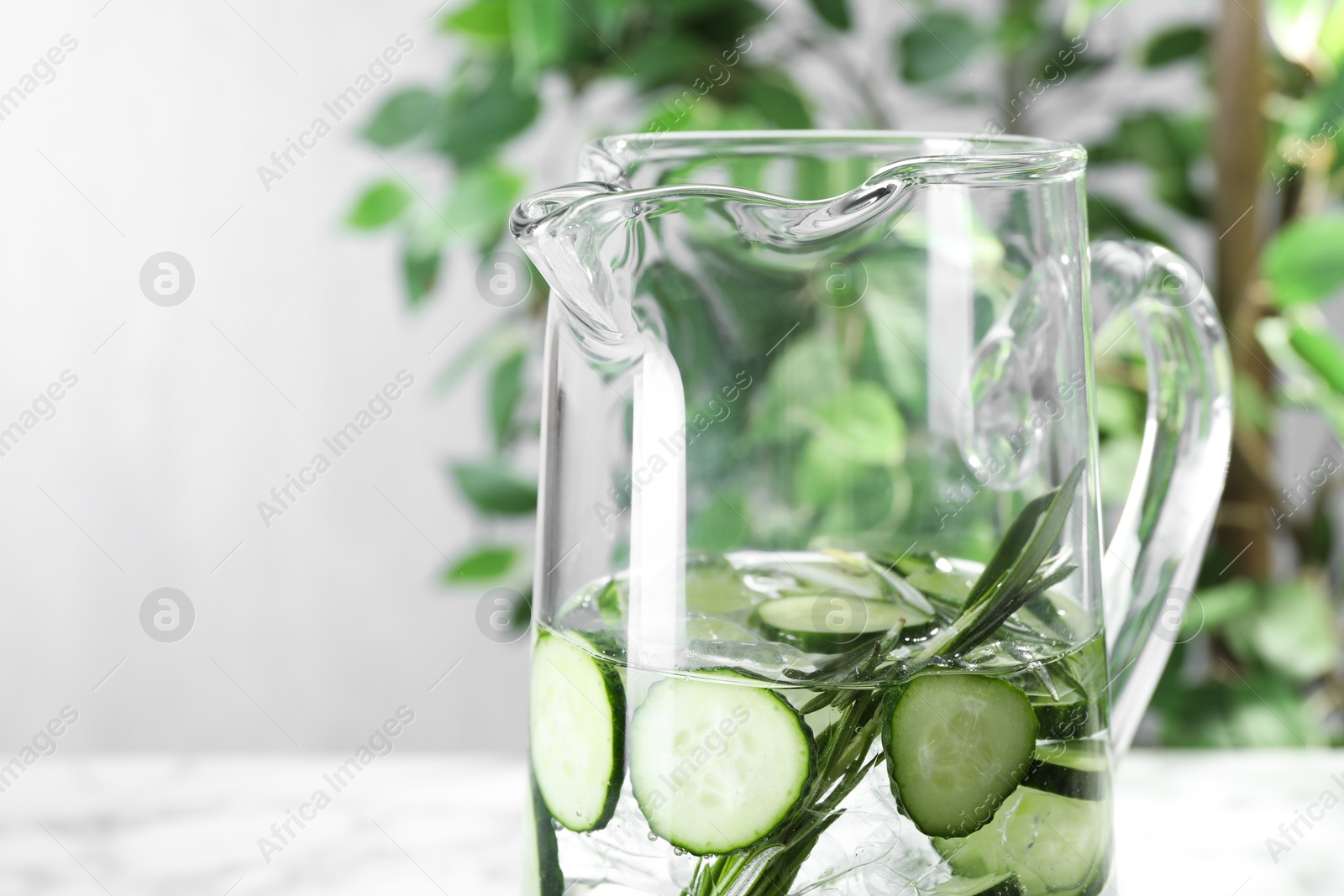 Photo of Refreshing cucumber water with rosemary in jug on blurred background, closeup. Space for text