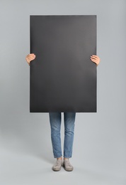Woman holding black blank poster on grey background. Mockup for design