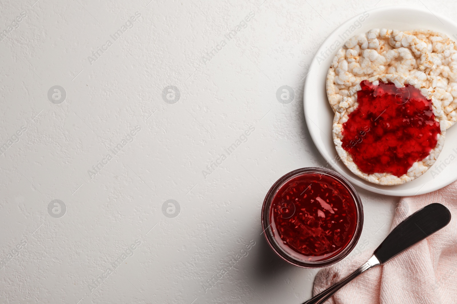 Photo of Homemade delicious raspberry jam on light table, flat lay. Space for text
