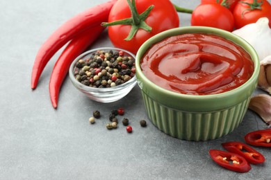 Photo of Bowl of tasty ketchup and ingredients on light grey table, closeup