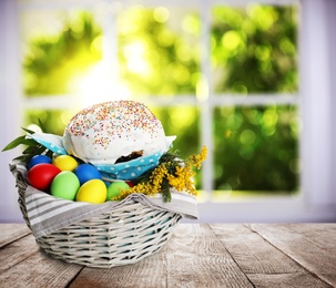 Basket with delicious Easter cake, dyed eggs and flowers on wooden table indoors. Space for text