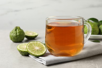 Glass cup of tasty bergamot tea and fresh fruits on light grey table