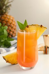 Tasty pineapple cocktail in glass and fresh fruit on white table