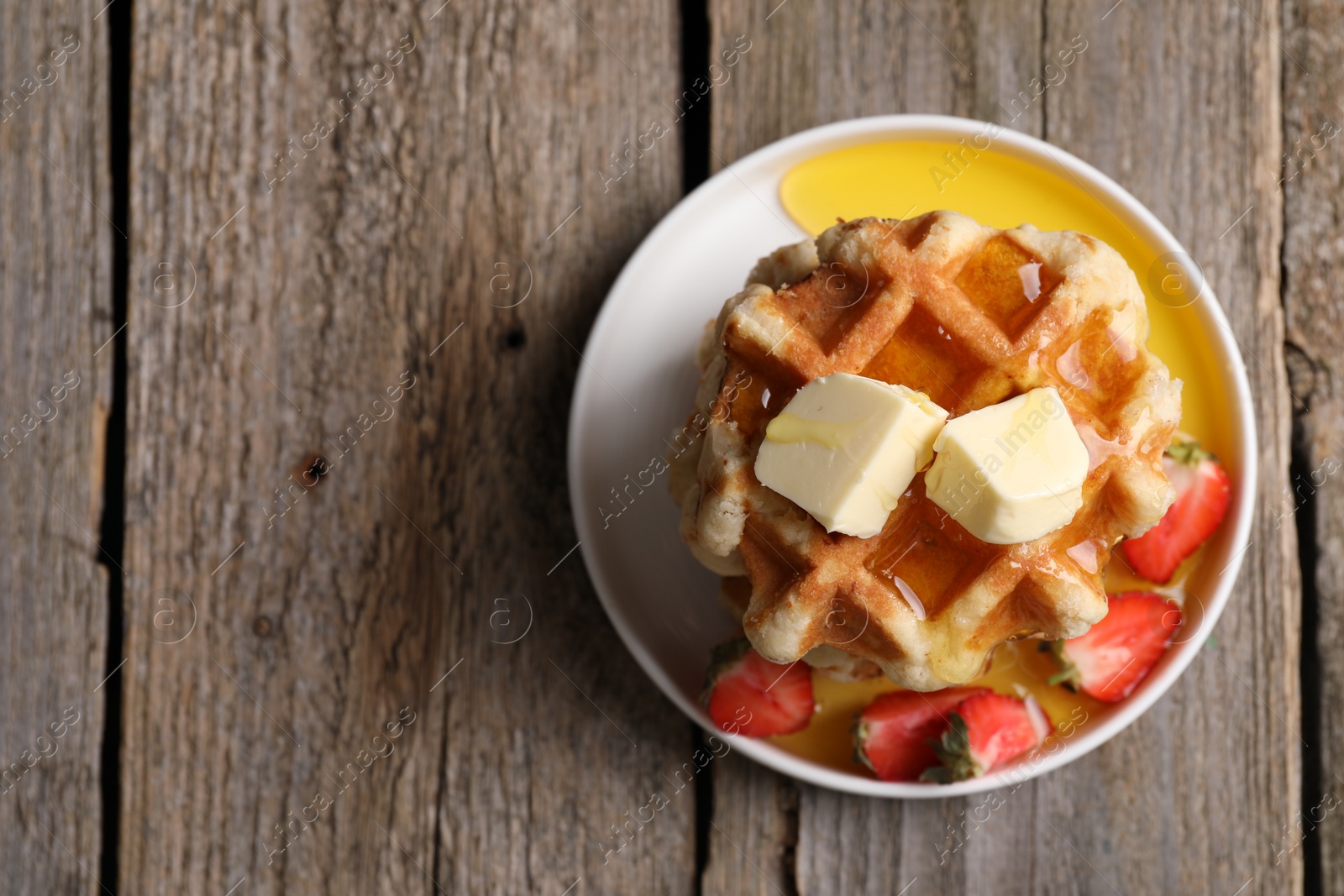 Photo of Delicious Belgian waffles with honey, butter and strawberries on wooden table, top view. Space for text