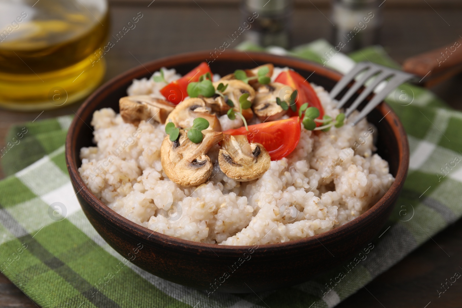 Photo of Delicious barley porridge with mushrooms, tomatoes and microgreens in bowl on table, closeup