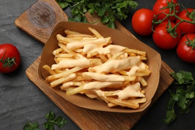 Photo of Tasty potato fries, cheese sauce in paper container and products on black table, top view