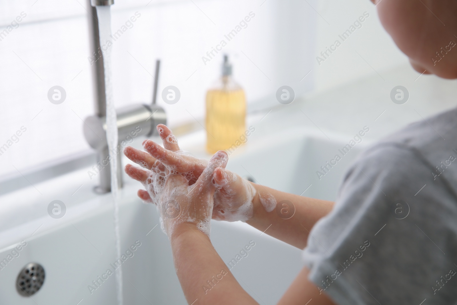 Photo of Little girl washing hands with liquid soap at home, closeup