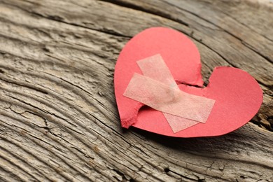 Photo of Broken heart. Torn red paper heart with medical adhesive bandages on wooden table, closeup with space for text