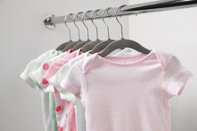 Photo of Baby bodysuits hanging on rack near white wall, closeup