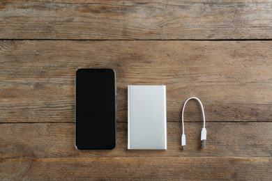 Photo of Mobile phone and portable charger on wooden background, flat lay