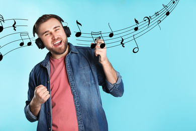 Handsome man listening to music via headphones on light blue background