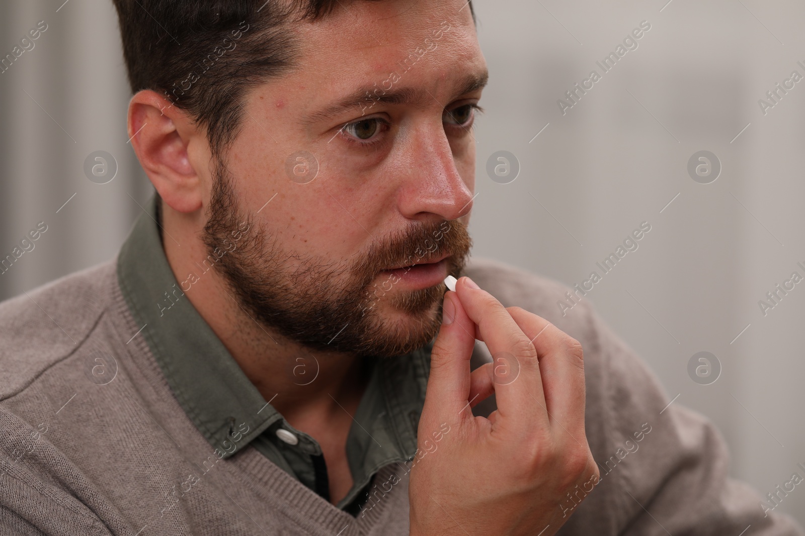 Photo of Depressed man taking antidepressant pill on light background, closeup