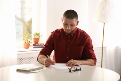 Man writing letter at white table in room