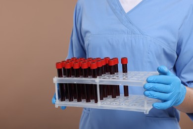 Laboratory testing. Doctor with blood samples in tubes on light brown background, closeup
