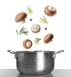 Fresh mushrooms, rosemary and peppercorns falling into pot on white background