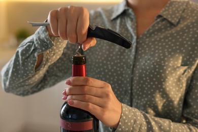 Photo of Woman opening wine bottle with corkscrew indoors, closeup