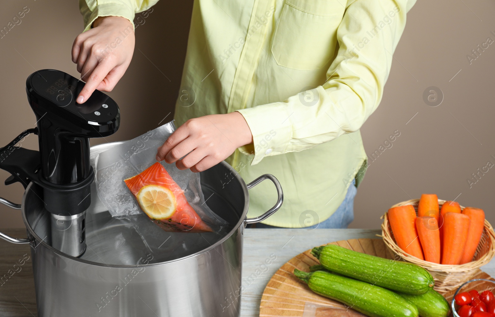 Photo of Woman putting vacuum packed salmon into pot and using thermal immersion circulator at table, closeup. Sous vide cooking