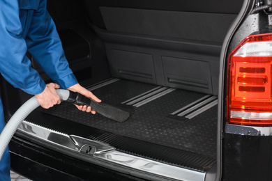 Worker using vacuum cleaner in automobile trunk at car wash, closeup