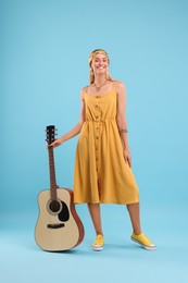 Happy hippie woman with guitar on light blue background
