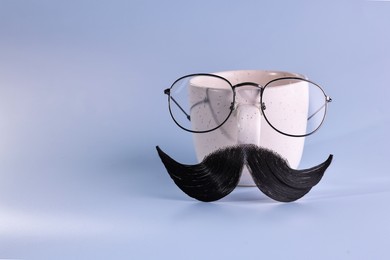 Photo of Man's face made of artificial mustache, glasses and cup on light blue background. Space for text