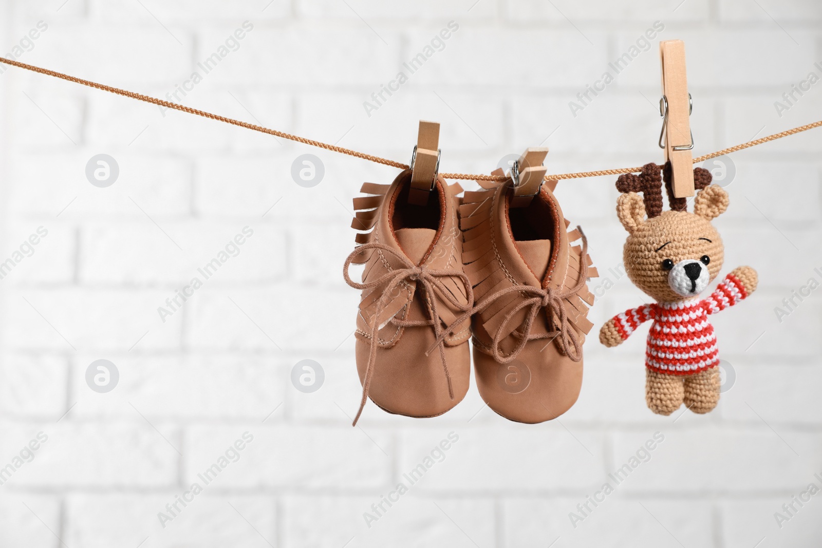 Photo of Cute baby shoes and crochet toy drying on washing line against white brick wall. Space for text