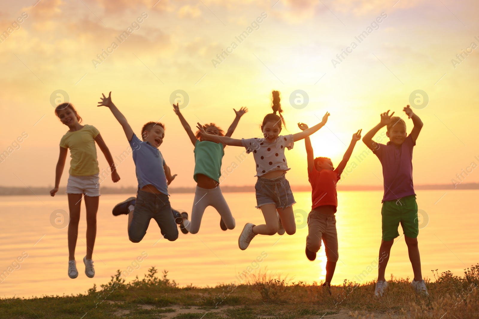 Image of Happy little children jumping near river at sunset