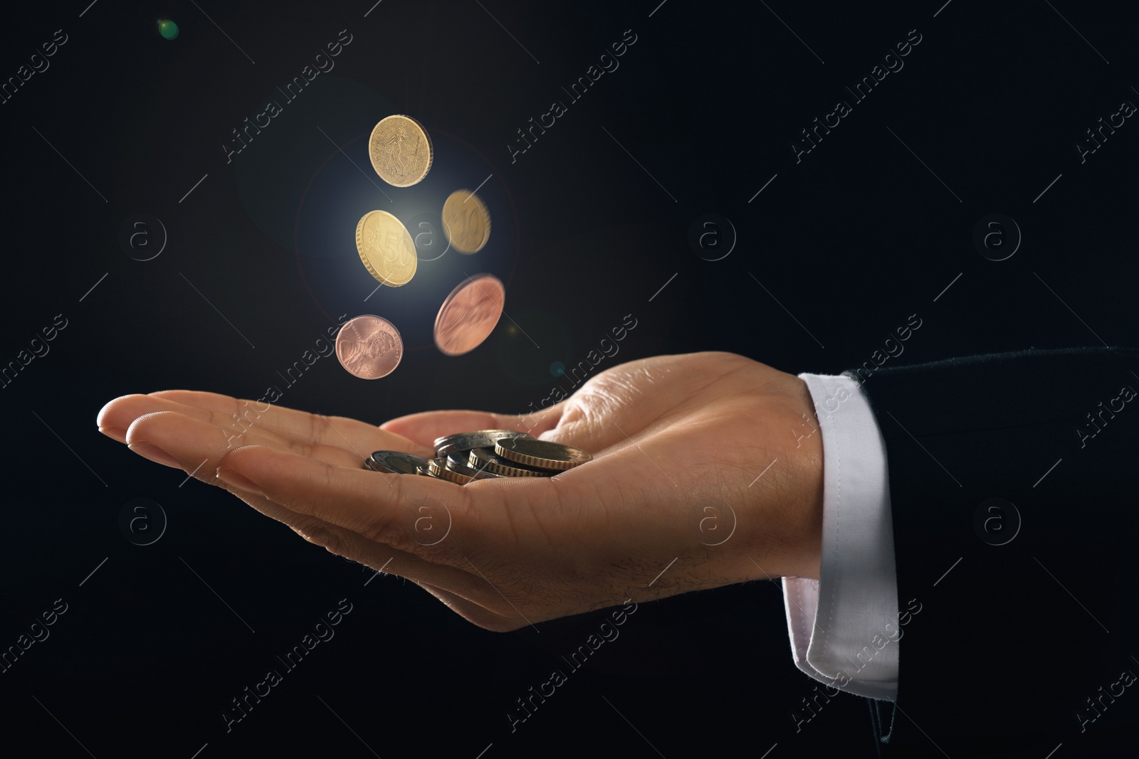 Image of Man and coins falling into his hand on black background, closeup