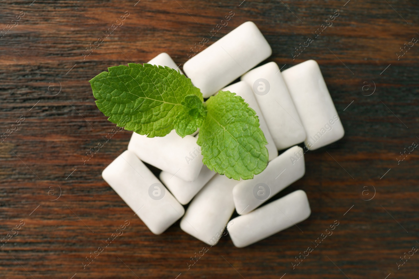 Photo of Tasty white chewing gums and mint leaves on wooden table, top view