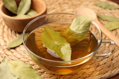 Photo of Cup of freshly brewed tea with bay leaves on wicker mat, closeup