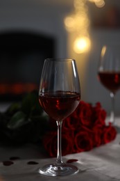 Photo of Glasses of red wine and rose flowers on grey table against blurred lights. Romantic atmosphere