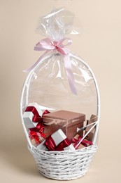 Photo of Wicker basket full of gift boxes on beige background