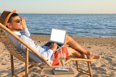 Photo of Happy man with laptop on deckchair near sea. Business trip