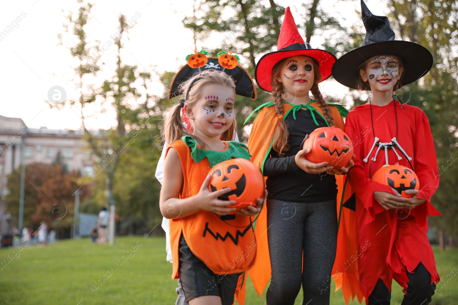 Photo of Cute little kids with pumpkin candy buckets wearing Halloween costumes in park