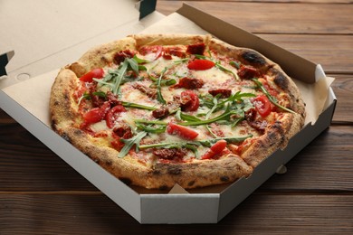 Photo of Tasty pizza with cheese, tomato and arugula in cardboard box on wooden table