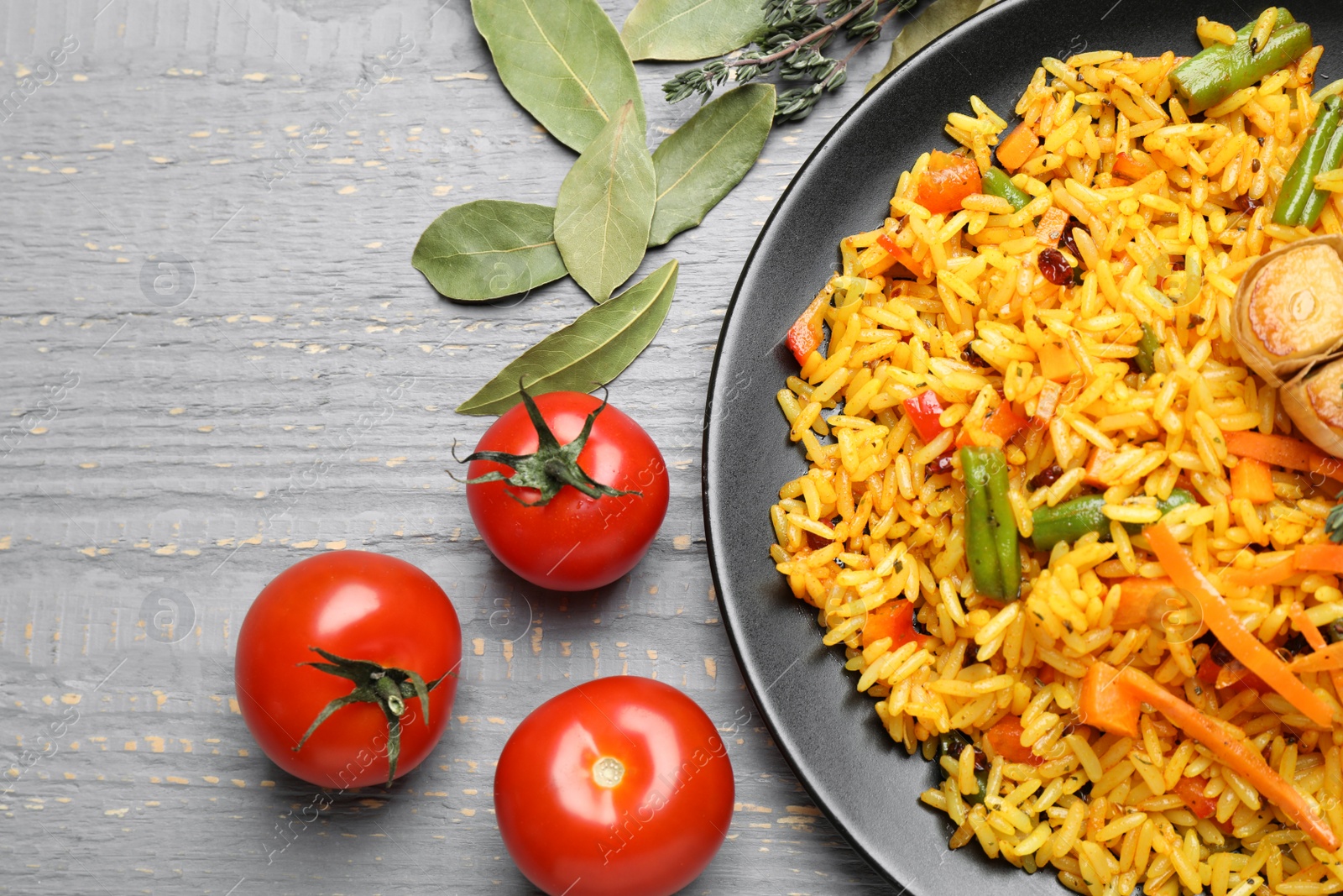 Photo of Tasty rice pilaf with vegetables on grey wooden table, flat lay